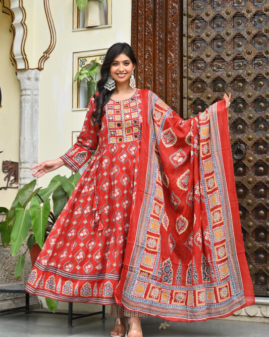 Woman wearing a red traditional outfit with a matching dupatta in an outdoor setting.